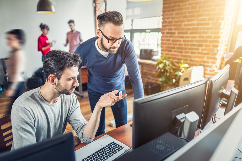 Two men collaborating on a project while looking at computer screens in a modern office.