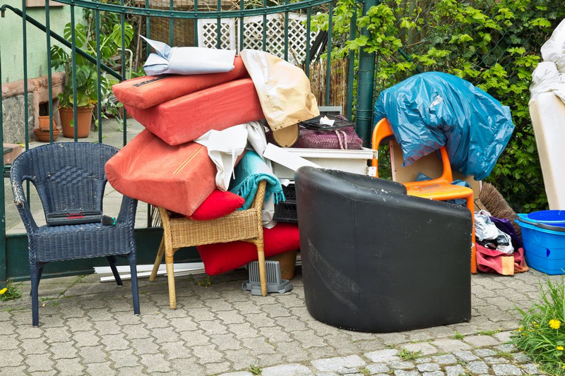 A pile of various household items, including furniture and cushions, stacked outside on a paved surface.