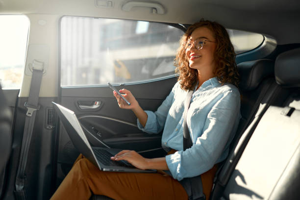 Businesswoman using laptop and phone in car, illustrating modern strategies for partnerships in the UAE.