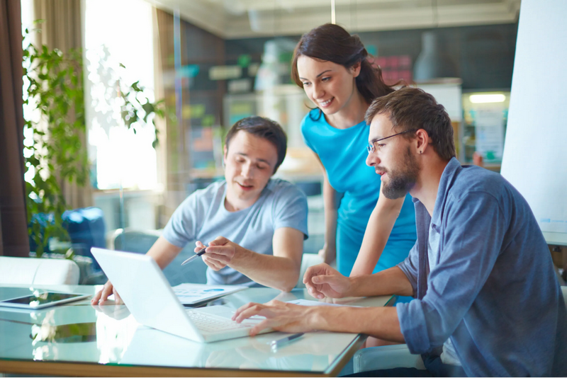 Three people collaborate at a table while looking at a laptop.