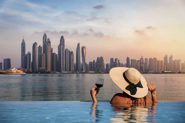 A person in a pool, overlooking the Dubai skyline while holding a glass of wine, symbolizes a luxurious lifestyle.